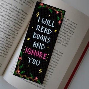 May include: A black bookmark with a white and pink floral design. The bookmark features the text "I will read books and ignore you".