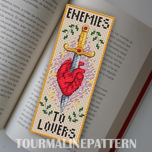 Bookmark on beige Aida: gold sword motif over a stylized red heart, purple hatch marks, green sprigs, and the phrase “ENEMIES TO LOVERS.” TourmalinePattern on Etsy