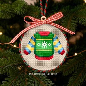 Christmas ornament cross stitch of a green sweater with snowflake in round hoop with red gingham ribbon on tree, TourmalinePattern on Etsy.