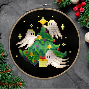 May include: A black and white cross-stitch embroidery design of three ghosts decorating a green Christmas tree with yellow stars and red ornaments.