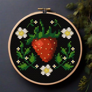 Può includere: Un cerchio da ricamo a punto croce con sfondo nero che presenta una fragola rossa con foglie verdi e fiori bianchi.