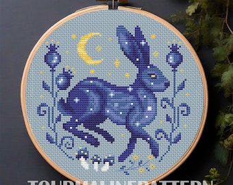 May include: Cross-stitch embroidery in a wooden hoop featuring a dark blue rabbit with white star-like details, a yellow crescent moon, and floral accents. The text "TOURMALINEPATTERN" is at the bottom. The design is on a light blue background.