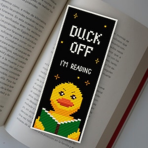 May include: A black bookmark with a yellow duck reading a green book. The bookmark has white stars and the text "Duck Off I'm Reading".
