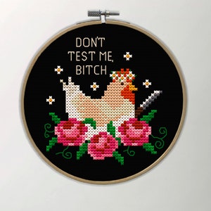 Puede incluir: Bordado de punto de cruz en un aro de madera. El dise&ntilde;o presenta una gallina con una corona floral y un cuchillo, rodeada de rosas rosas y hojas verdes. El texto "DON'T TEST ME, BITCH" est&aacute; bordado encima de la gallina.