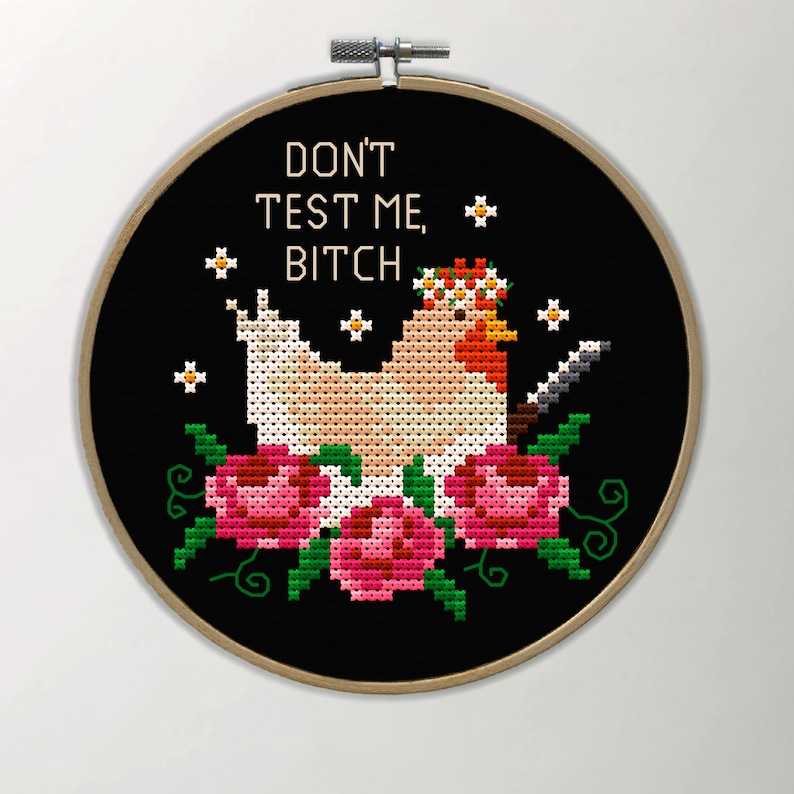 Puede incluir: Bordado de punto de cruz en un aro de madera. El dise&ntilde;o presenta una gallina con una corona floral y un cuchillo, rodeada de rosas rosas y hojas verdes. El texto "DON'T TEST ME, BITCH" est&aacute; bordado encima de la gallina.