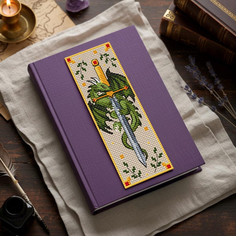 Cross-stitch bookmark with a green dragon coiled around a silver longsword; gold hilt with red gems, ivy sprigs, small gold stitches, and a yellow border on beige fabric—vertical fantasy design for readers. TourmalinePattern on Etsy