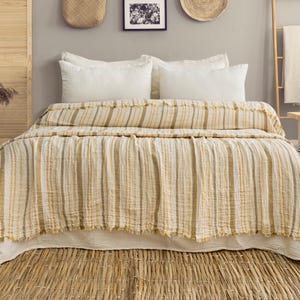 Pu&ograve; includere: Un letto con un piumino a righe gialle e bianche e cuscini bianchi. Il letto &egrave; fatto con un copriletto strutturato e con frange. La stanza ha una palette di colori neutri con accenti in legno naturale e un tappeto tessuto.