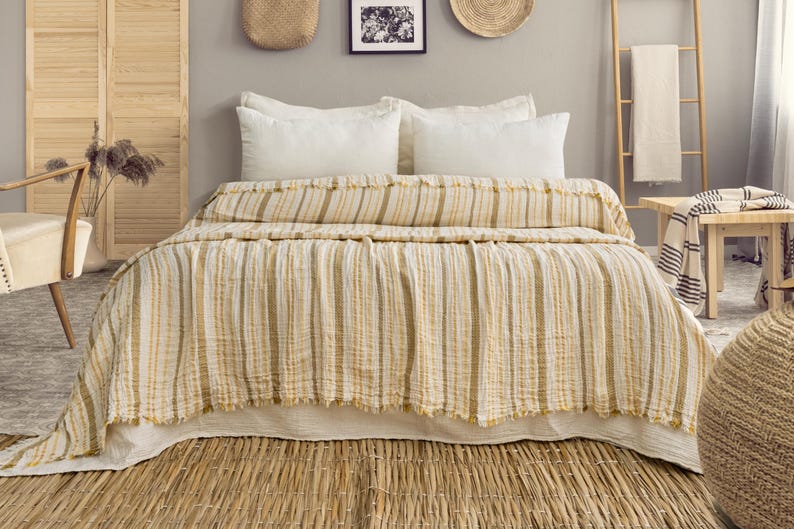 Pu&ograve; includere: Un letto con un piumino a righe gialle e bianche e cuscini bianchi. Il letto &egrave; fatto con un copriletto strutturato e con frange. La stanza ha una palette di colori neutri con accenti in legno naturale e un tappeto tessuto.