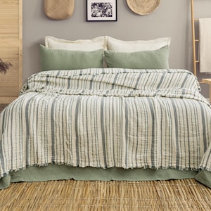 Pu&ograve; includere: Un letto con una trapunta a righe bianche e grigie, completata da cuscini verdi e un copriletto verde. La stanza presenta una scala di legno, un tavolino di legno e decorazioni murali, creando un ambiente camera da letto accogliente.
