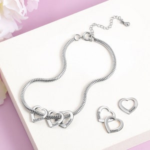 Pode incluir: Pulseira de corrente prateada com cinco pingentes de coração entrelaçados, cada um gravado com um nome: Matthew, Isaac, Jayden, Elijah e Sa'vey.