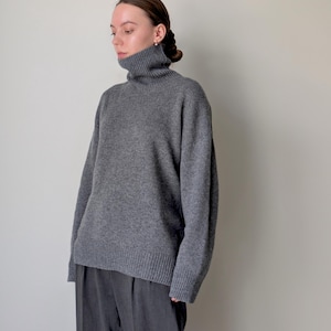 Op de afbeelding: Een antracietgrijze trui met lange mouwen, een hoge col, verlaagde schouders en geribbelde gebreide details bij de manchetten en de zoom, gecombineerd met een donkergrijze broek met een zichtbare verticale vouw aan de voorzijde.