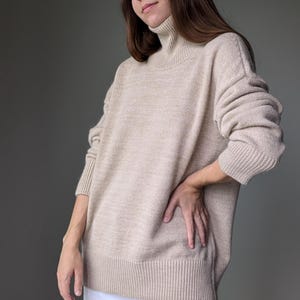 May include: A beige turtleneck sweater with long sleeves and a ribbed hem.