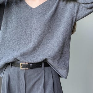 Puede incluir: Un su&eacute;ter gris de cuello en V con mangas largas y un cintur&oacute;n de cuero negro.