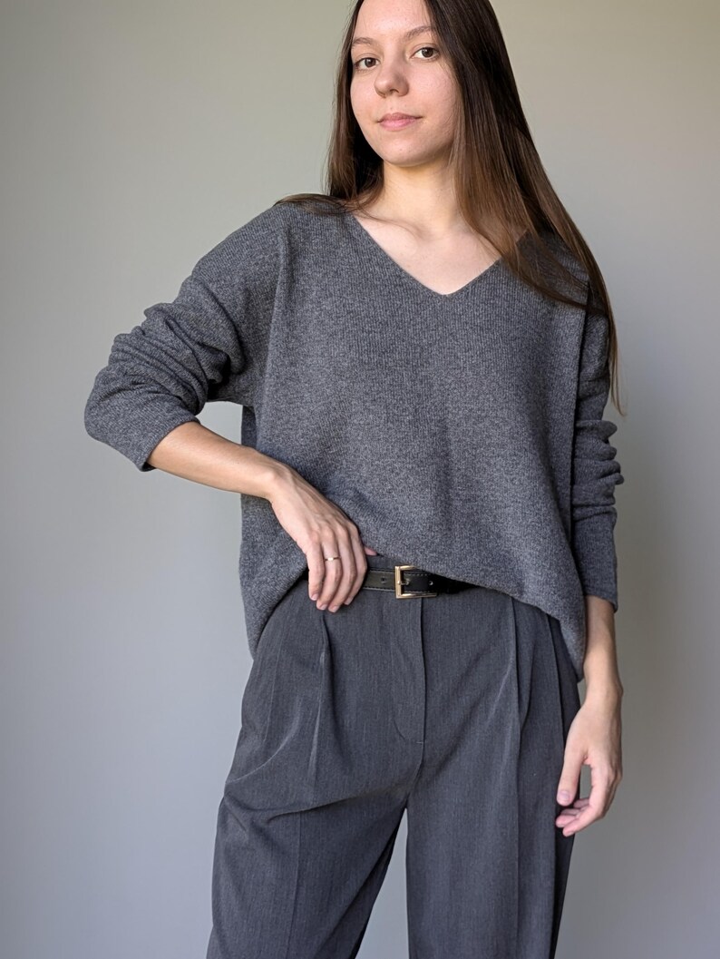 Puede incluir: Un su&eacute;ter gris de cuello en V con mangas largas y un cintur&oacute;n gris. El su&eacute;ter se lleva sobre pantalones grises.