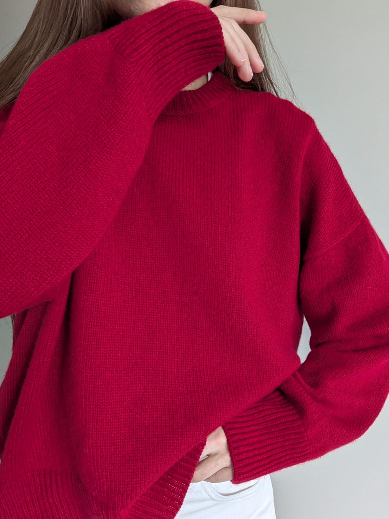 May include: A long-sleeved, solid deep red sweater featuring a ribbed crew neckline, ribbed cuffs, and a ribbed hem. The knit garment has a relaxed fit with dropped shoulders and a consistent, fine-textured weave throughout the entire piece.