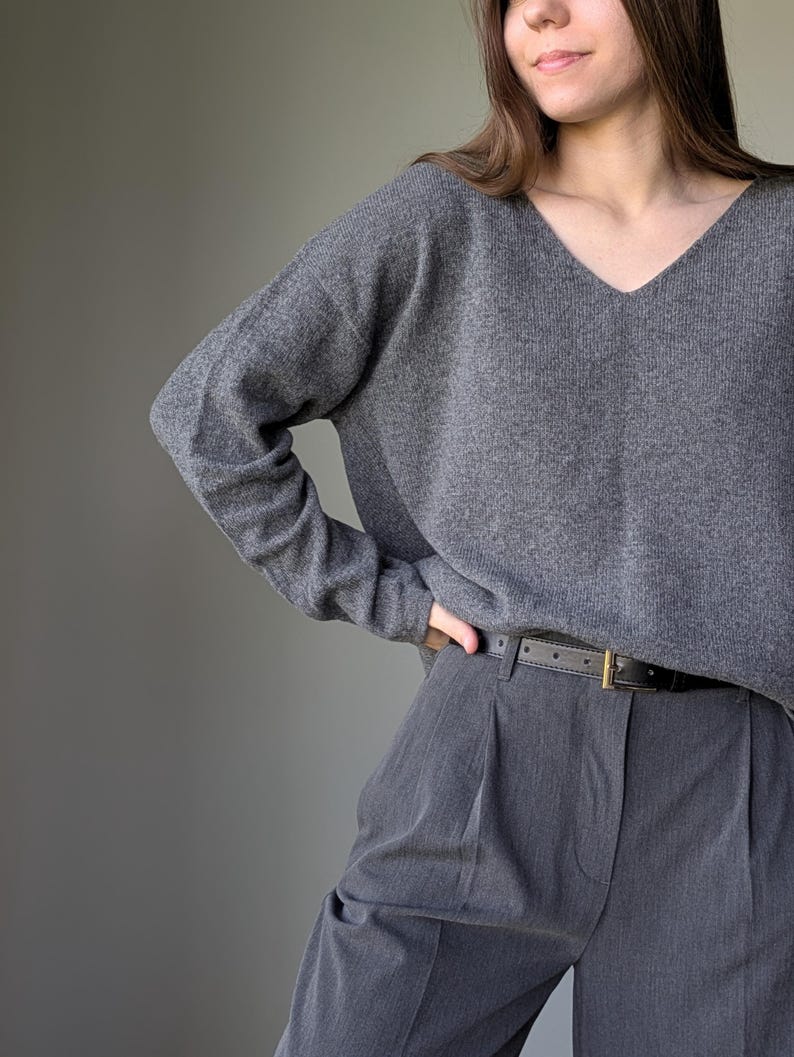 Puede incluir: Un su&eacute;ter gris de cuello en V con mangas largas y un pantal&oacute;n gris de pinzas con un cintur&oacute;n negro.