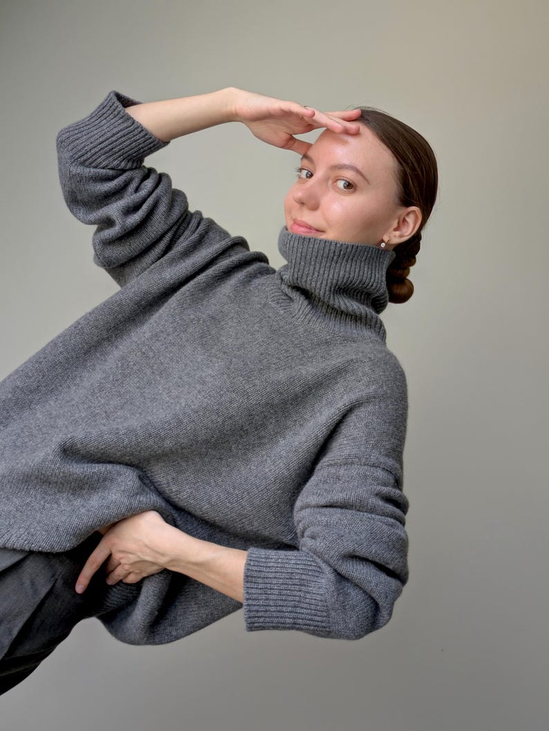 Op de afbeelding: Een antracietgrijze gebreide trui met een hoge col, lange mouwen met geribbelde boorden en een relaxte, oversized pasvorm. Het kledingstuk is gemaakt van een zacht, gestructureerd wolmengsel met een consistente gem&ecirc;leerde uitstraling.