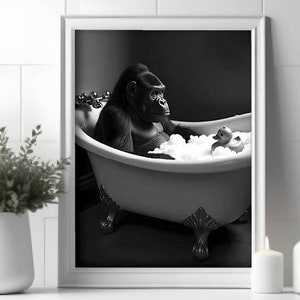 Puede incluir: Una fotografía en blanco y negro de un gorila tomando un baño en una bañera blanca con burbujas. El gorila está sentado en la bañera con un pato de goma flotando en el agua.