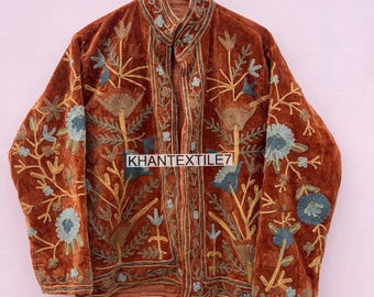 Op de afbeelding: Bruine fluwelen jas met ingewikkelde bloemenborduurwerk in blauw en goud. De jas heeft een hoge kraag en hangt aan een houten hanger. De tekst "KHANTEXTILE7" is zichtbaar op de voorkant.