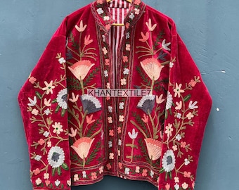 May include: A red velvet jacket with floral embroidery. The jacket features a high collar and a striped lining. The embroidery includes pink, white, and gray flowers with green stems and leaves. The text "KHANTEXTILE7" is visible on the jacket.