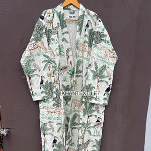May include: A long, open-front robe with a white background and a repeating pattern of zebras, leopards, birds, and palm trees in green and tan. The robe is hanging on a wooden hanger.