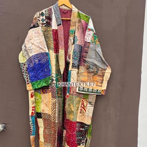 Könnte beinhalten: Ein Patchwork-Robe mit einer Vielzahl von bunten Stoffquadraten. Die Robe hat lange Ärmel und hängt an einem Holzbügel. Der Text "KHANTEXTILE7" ist auf der Vorderseite der Robe zu sehen.