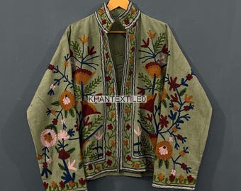 May include: Olive green jacket with intricate floral embroidery in shades of orange, pink, and blue. The jacket features a mandarin collar and is displayed on a wooden hanger. The text "KHANTEXTILEO" is visible on the jacket.