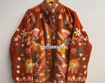 May include: Rust-colored velvet jacket with intricate floral embroidery in shades of pink, yellow, and white. The jacket features a high collar and is adorned with the text "KHANTEXTILE7". The embroidery creates a detailed, textured design.