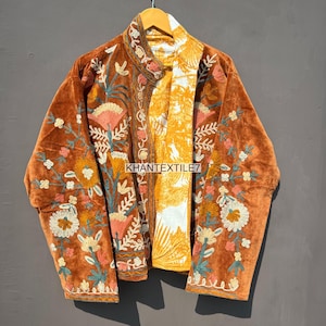 Può includere: Giacca in velluto marrone con ricami floreali nei toni dell'arancione, rosa e verde. La giacca ha un colletto alla coreana e una fodera a fantasia gialla e bianca. Il testo "KHANTEXTILE7" è visibile sulla giacca.