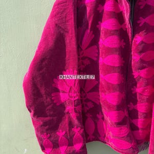 May include: A magenta jacket with a floral pattern in a brighter shade of pink. The jacket has a zipper closure and the text "KHANTEXTILE7" is visible. The jacket is made of a soft, velvety material.