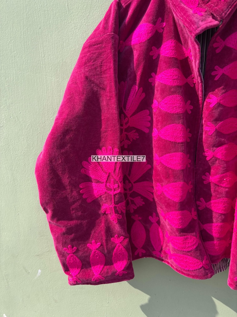 May include: A magenta jacket with a floral pattern in a brighter shade of pink. The jacket has a zipper closure and the text "KHANTEXTILE7" is visible. The jacket is made of a soft, velvety material.