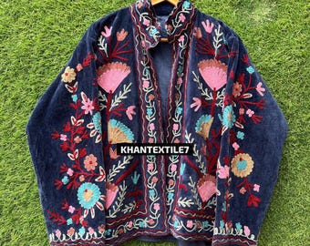 Può includere: Giacca in velluto blu navy con ricami floreali colorati. La giacca presenta fiori e foglie ricamati rosa, rossi, turchese e oro. Il testo "KHANTEXTILE7" è visibile sulla parte anteriore della giacca.