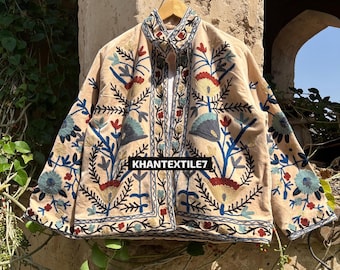 Puede incluir: Chaqueta beige bordada con motivos florales y de hojas en azul, rojo y amarillo. La chaqueta tiene cuello alto y cierre de botones. El texto "KHANTEXTILE7" es visible.