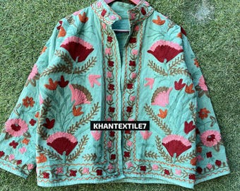 May include: A light teal jacket with intricate floral embroidery in shades of burgundy, pink, and orange. The jacket features a mandarin collar and long sleeves. The text "KHANTEXTILE7" is visible on the lower part of the jacket.
