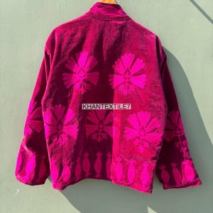 May include: A magenta velvet jacket with bright pink floral embroidery. The jacket features a high collar and long sleeves. The back of the jacket displays large floral designs and the text "KHANTEXTILE7".