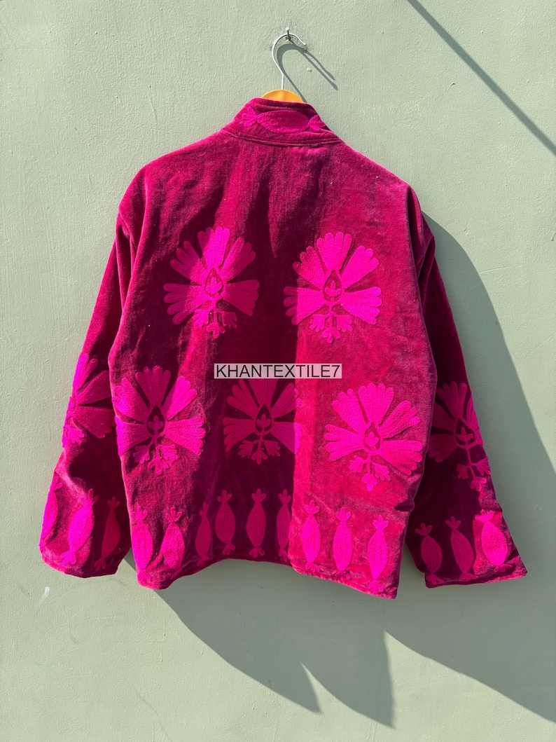 May include: A magenta velvet jacket with bright pink floral embroidery. The jacket features a high collar and long sleeves. The back of the jacket displays large floral designs and the text "KHANTEXTILE7".