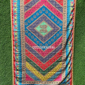 Peut inclure: Textile coloré avec un motif géométrique. Le textile présente un motif de losange central dans les tons de bleu, rose, rouge et jaune, avec des accents dorés. Les bords sont bordés d'une bordure dorée et le texte "KHANTEXTILE7" est visible.