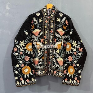 May include: Black jacket with detailed floral embroidery in orange, pink, and cream. The jacket has a high collar and features the text "KHANTEXTILE7". The embroidery is intricate and covers the front and sleeves.