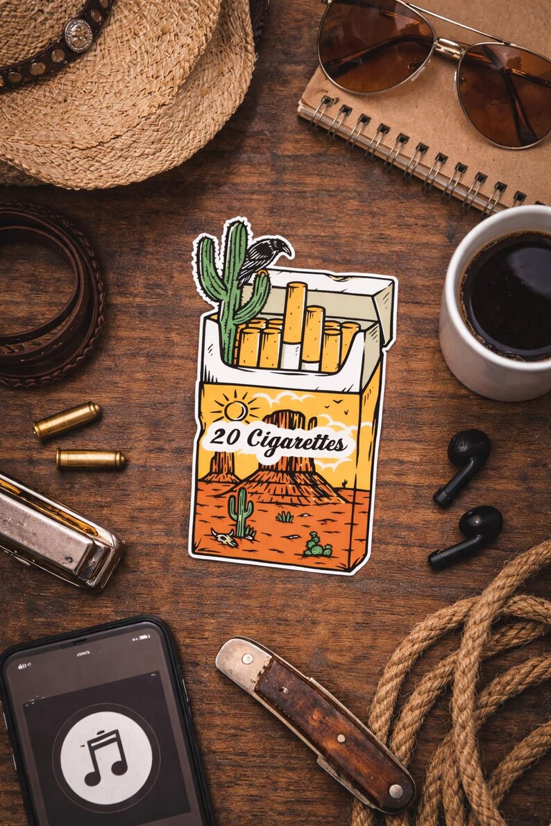 Puede incluir: Una pegatina de un paquete de cigarrillos con un dise&ntilde;o de paisaje des&eacute;rtico, con un cactus y un cuervo. Se muestra el texto "20 Cigarettes". La imagen est&aacute; rodeada por un sombrero de vaquero, gafas de sol y otros accesorios.
