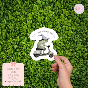 Könnte beinhalten: Aufkleber mit einem grünen Frosch mit Hexenhut und Brille auf einem Roller. Der Text "Off to commit tom foolery" steht darüber. Erhältlich als Vinyl-Aufkleber, Kühlschrankmagnet und Magnet-Lesezeichen.