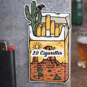 Puede incluir: Una pegatina con una escena des&eacute;rtica con un paquete de cigarrillos. El paquete lleva la inscripci&oacute;n "20 Cigarettes" y tiene un cactus y un cuervo. El fondo muestra un paisaje des&eacute;rtico con monta&ntilde;as y cactus.