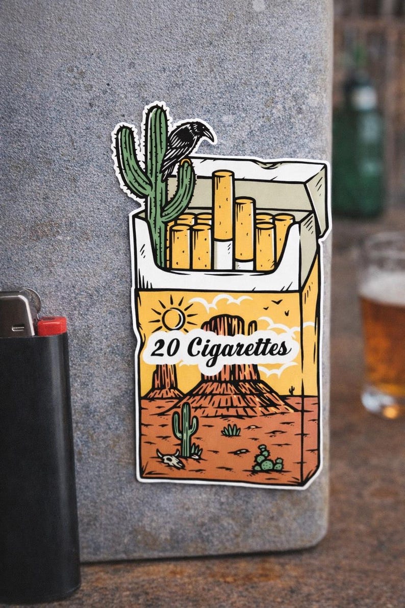Puede incluir: Una pegatina con una escena des&eacute;rtica con un paquete de cigarrillos. El paquete lleva la inscripci&oacute;n "20 Cigarettes" y tiene un cactus y un cuervo. El fondo muestra un paisaje des&eacute;rtico con monta&ntilde;as y cactus.