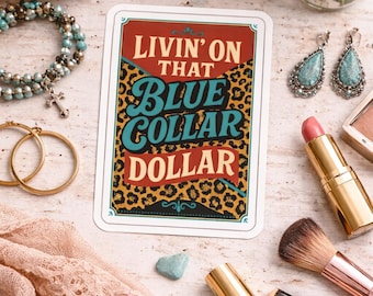 Puede incluir: Una variedad de accesorios y productos de belleza se disponen sobre una superficie clara. Un letrero decorativo con el texto "Livin' on that Blue Collar Dollar" es el punto focal. Otros elementos incluyen un sombrero de paja, joyas, brochas de maquillaje y lápiz labial.