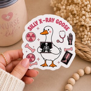 May include: A white sticker featuring a cartoon goose holding an X-ray image. The sticker has the text "SILLY X-RAY GOOSE" in pink, along with medical-themed illustrations like a stethoscope, bones, and radiation symbols. The goose has orange feet and a beak.