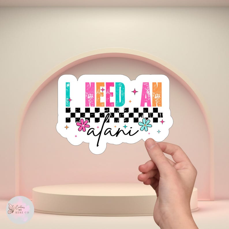 Puede incluir: Una pegatina blanca con el texto "I NEED AN afari" en letras coloridas y desgastadas. El dise&ntilde;o incluye un patr&oacute;n de tablero de ajedrez en blanco y negro, flores y estrellas. La pegatina est&aacute; sujeta por una mano.
