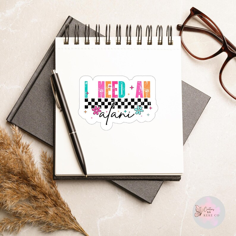 Puede incluir: Una pegatina colorida con el texto "I NEED AN afani" en una fuente retro. El dise&ntilde;o incluye un borde a cuadros y detalles florales. Se encuentra sobre un bloc de notas blanco con un bol&iacute;grafo negro, un cuaderno negro y gafas.