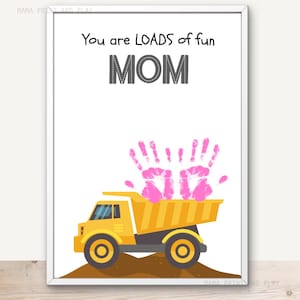 Puede incluir: Impresión enmarcada con las palabras "You are LOADS of fun MOM". La imagen presenta un camión volquete amarillo con huellas de manos rosas en la caja. La impresión está sobre un fondo blanco.