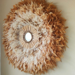 Peut inclure: Miroir mural rond avec un design de plumes naturelles. Le miroir est entouré d'un arrangement circulaire de plumes marron clair et blanches. Le miroir central est petit et rond, encadré par une bordure tressée en forme de soleil.