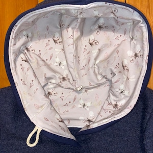 May include: A navy blue hoodie with a white drawstring and a pink floral lining featuring a butterfly pattern.