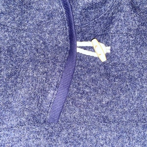 May include: A close-up of a blue sweater with a white toggle closure.